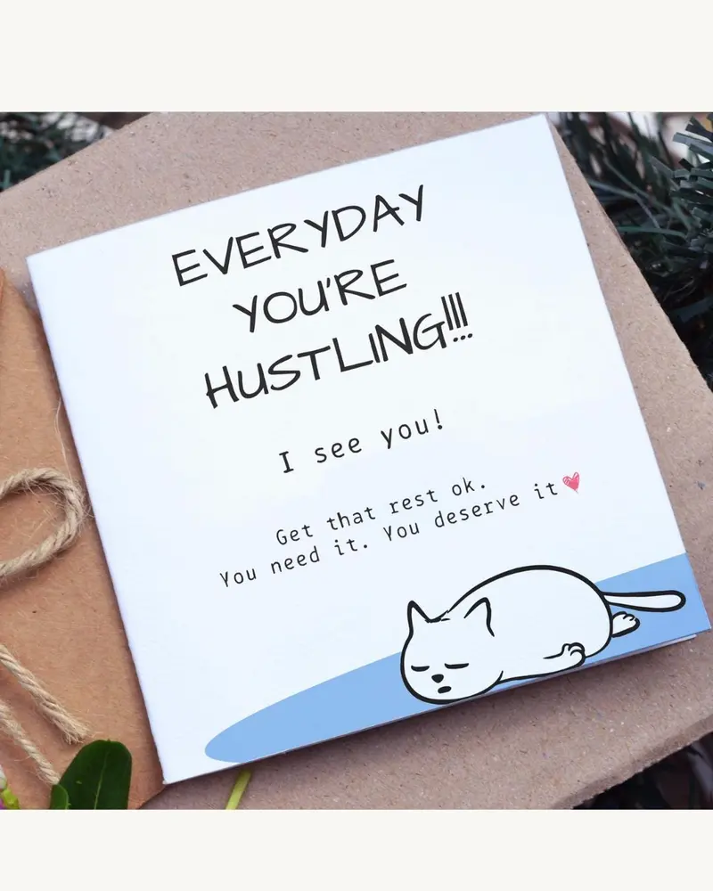 A white greeting card with the text "EVERYDAY YOU'RE HUSTLING!!!" and "I see you!" A cartoon cat is 