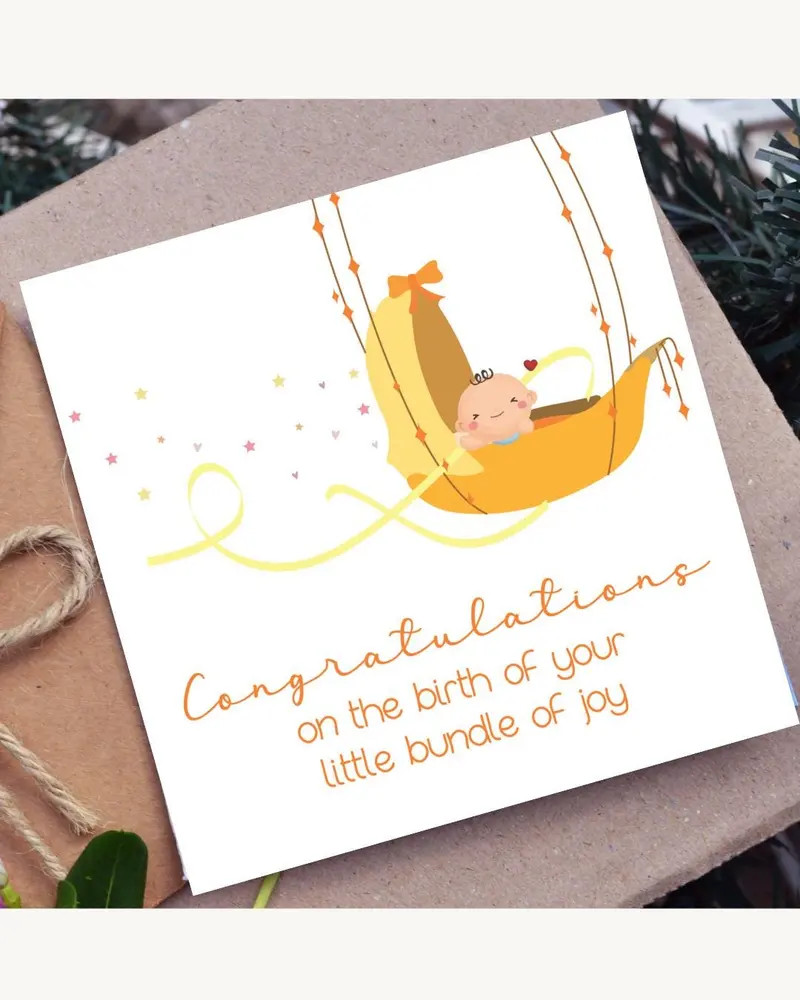 A baby-themed greeting card. The illustration shows a cartoon baby in a yellow cradle. The card has 
