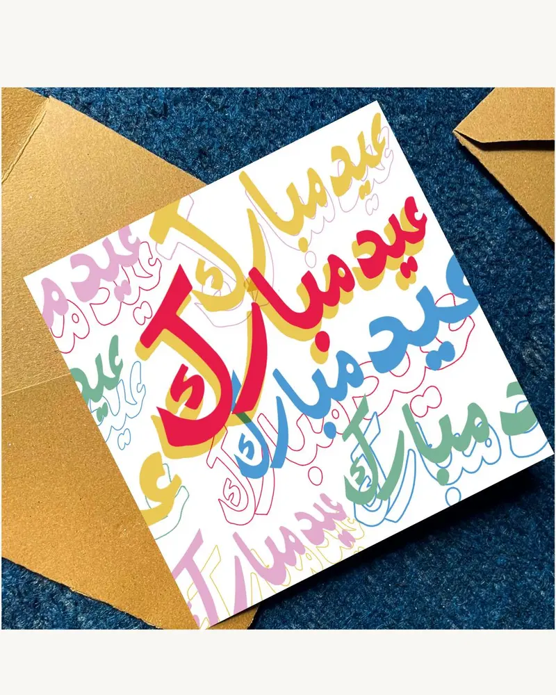 A white greeting card with colourful Arabic calligraphy saying "Eid Mubarak" in red, yellow, blue, a