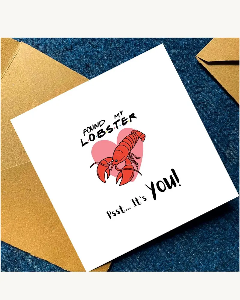A square white greeting card featuring a red lobster illustration centred over a pink heart. The tex